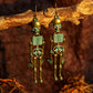 Two antique bronze skeleton earrings with teal accents hang from a branch.