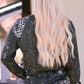 A woman from behind wearing a black long-sleeve t-shirt with white splatters and light blue jeans.