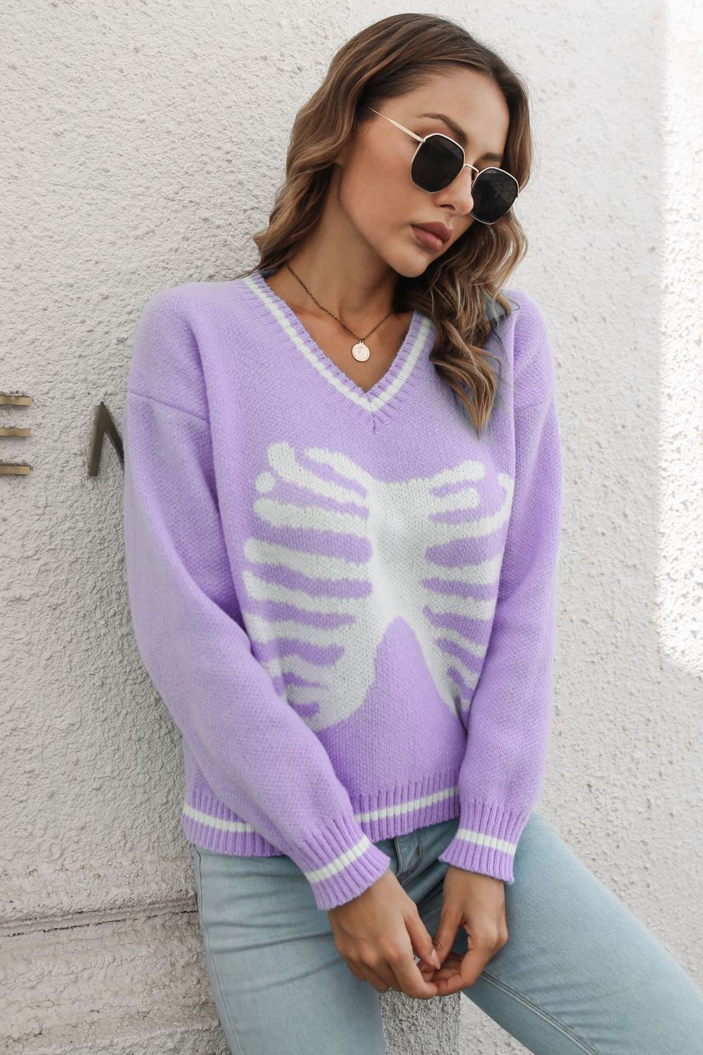 A woman wears a purple skeleton pattern v-neck long sleeve pullover sweater.
