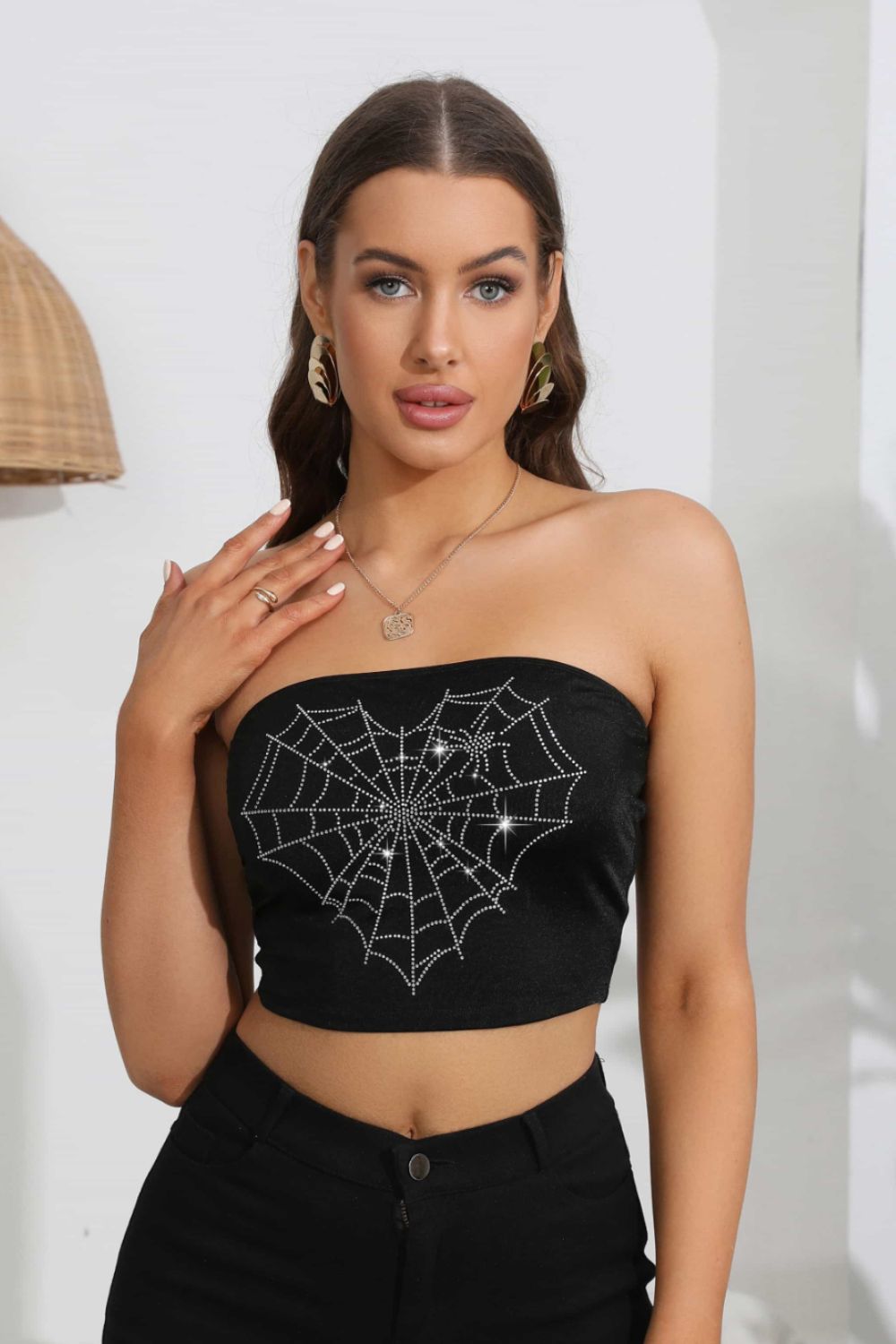 A woman models a black tube top with a rhinestone heart spider web graphic.