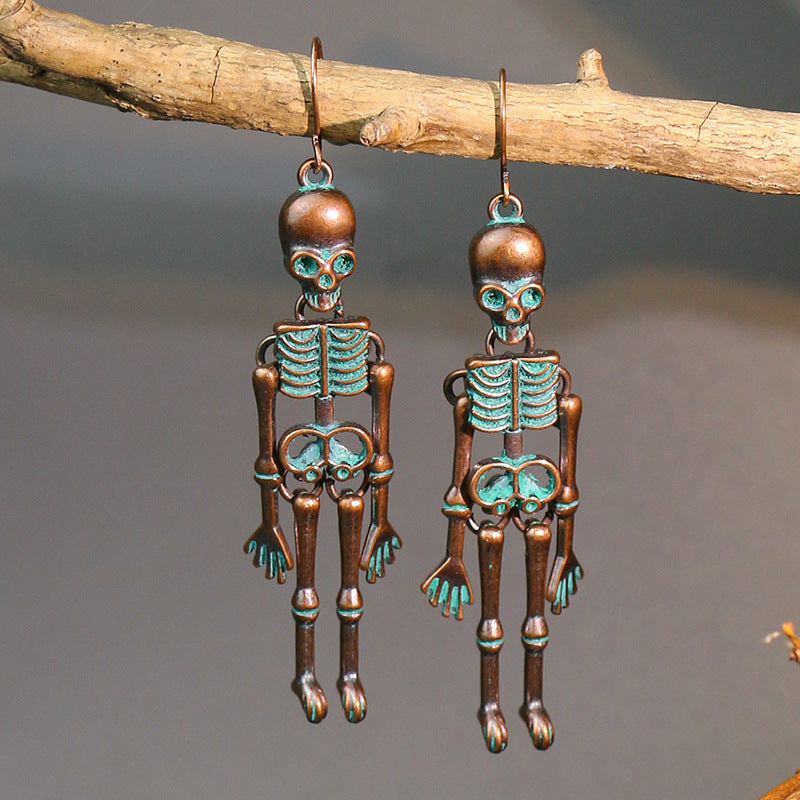 Two antique copper-colored skeleton earrings with teal accents hang from a branch.