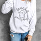 White long-sleeve sweatshirt with "spooky season" ghost graphic, worn with ripped jeans.