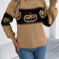 A woman wears a tan long-sleeve sweater with a black pumpkin pattern and blue jeans.