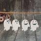 Four ghost-shaped dangle earrings hang from a wooden branch.