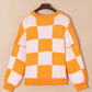 Pumpkin checkered round neck long sleeve sweater on a hanger.