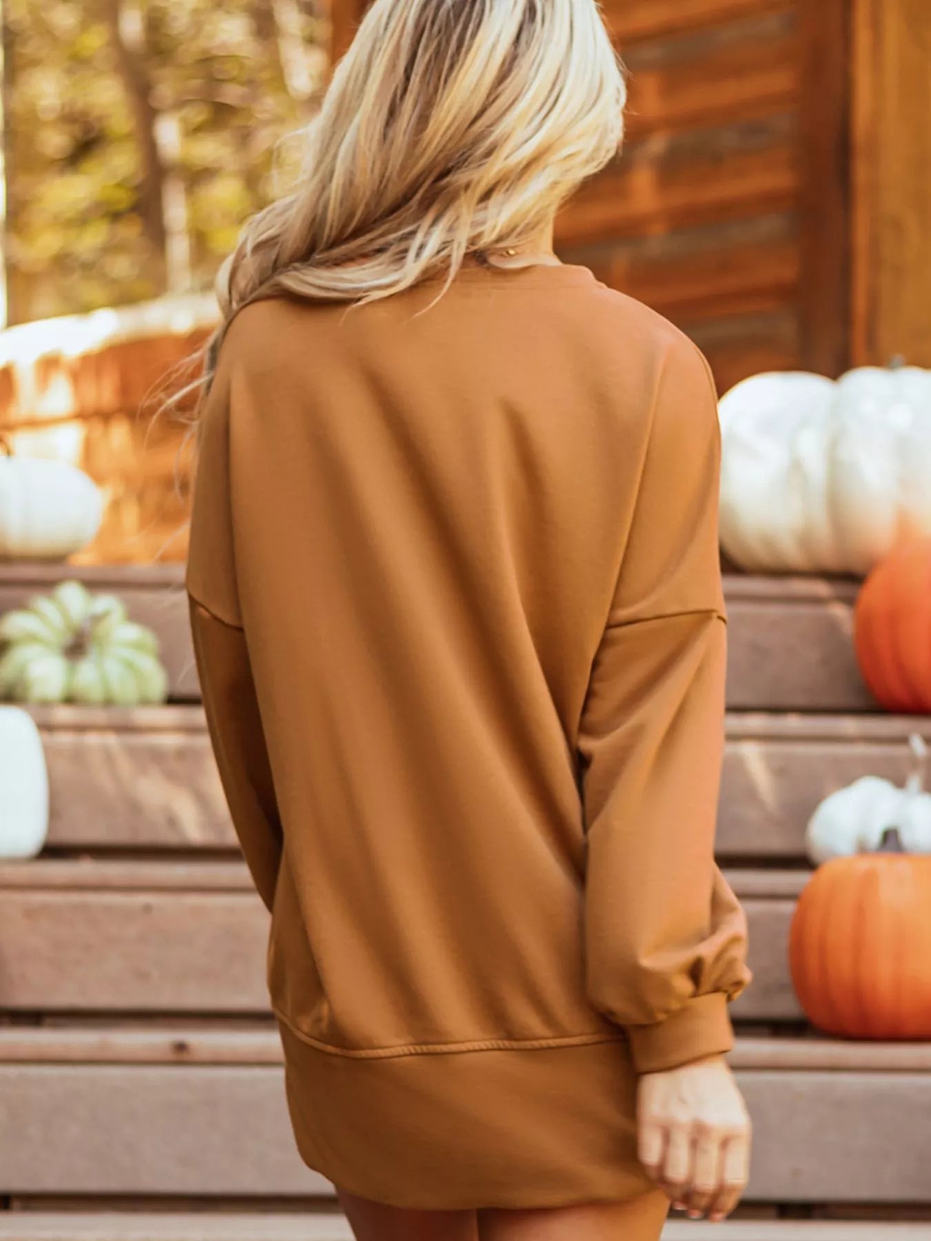 Blonde woman from behind wearing a loose, long-sleeve, brown top.