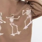 An oversized brown sweatshirt features three white skeleton graphics skateboarding.