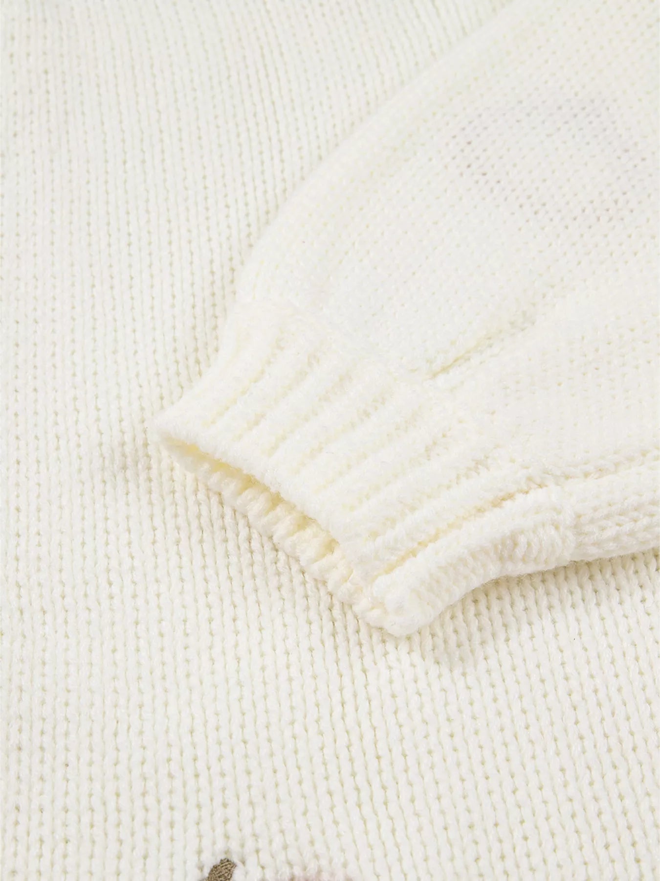 Close-up of a cream knit cardigan sleeve with a ribbed cuff.