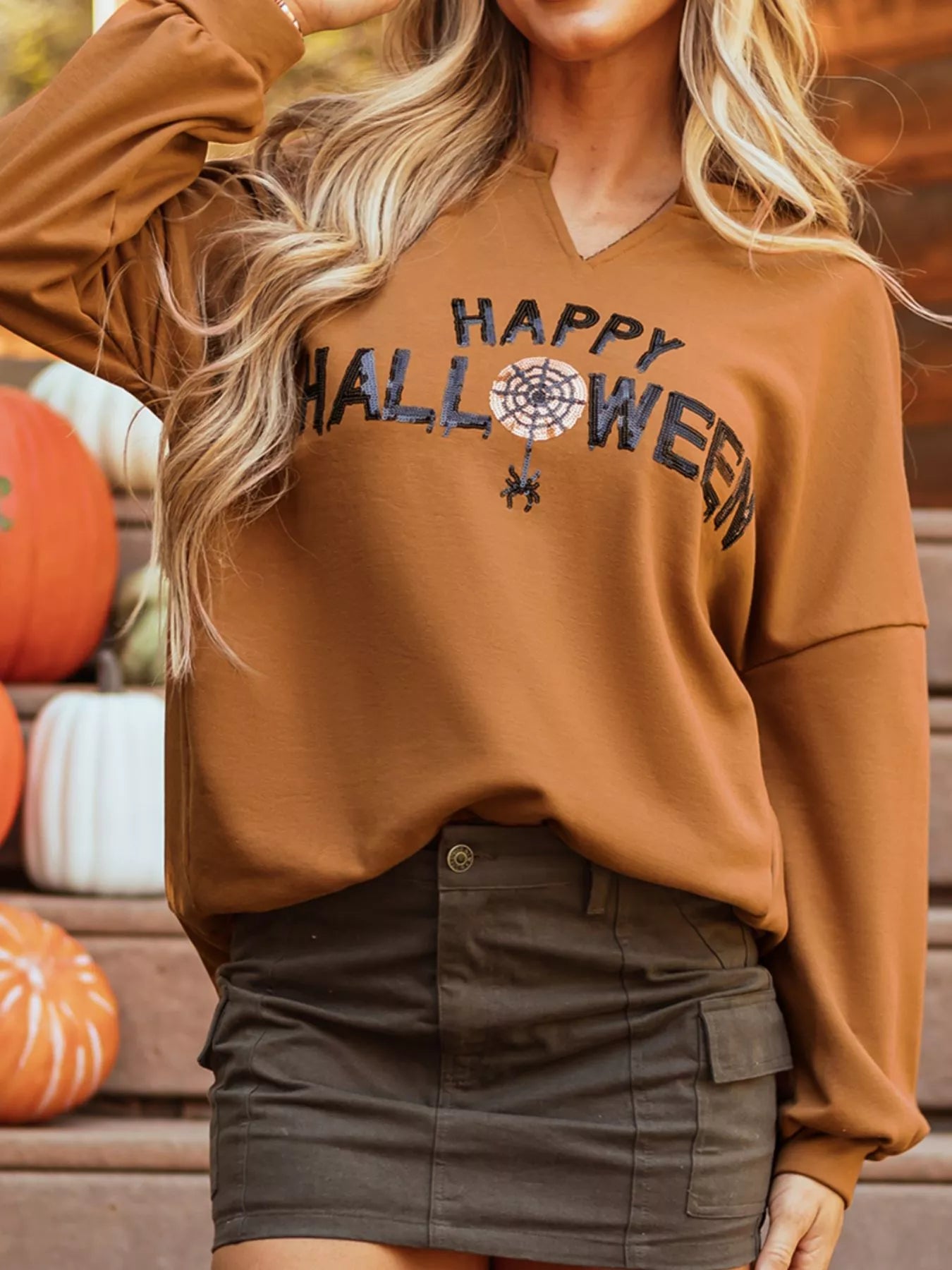 A woman wears a brown long-sleeve top with "Happy Halloween" text and a spiderweb graphic.