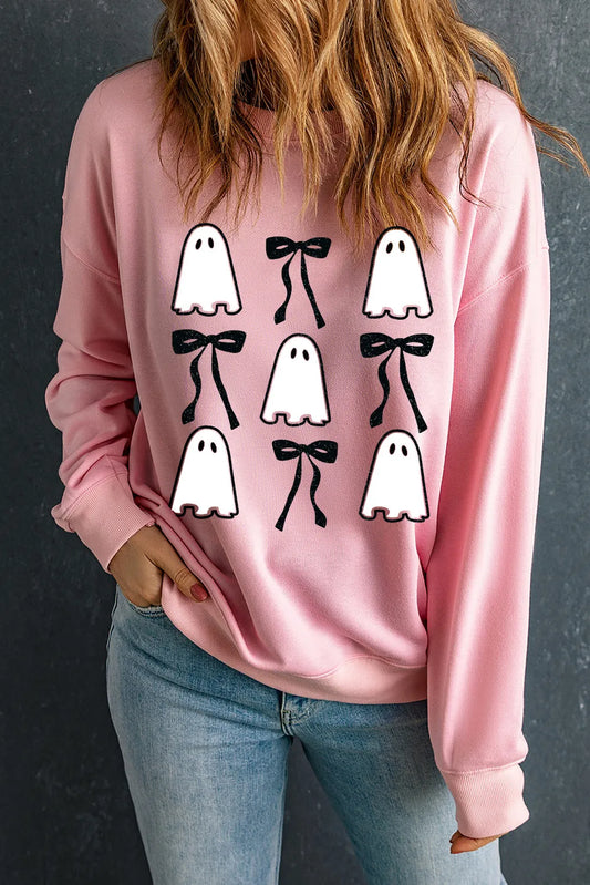 A woman wears a pink sweatshirt with ghost and bow designs.