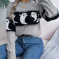 A woman wears a gray round neck long sleeve sweater with a black and white ghost pattern.