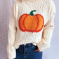 A cream cable-knit turtleneck sweater with a large orange pumpkin applique.