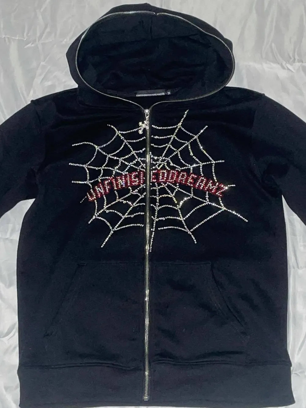 Black zip-up hoodie with a rhinestone spider web design and "UNFINISHEDDREAMZ" text.