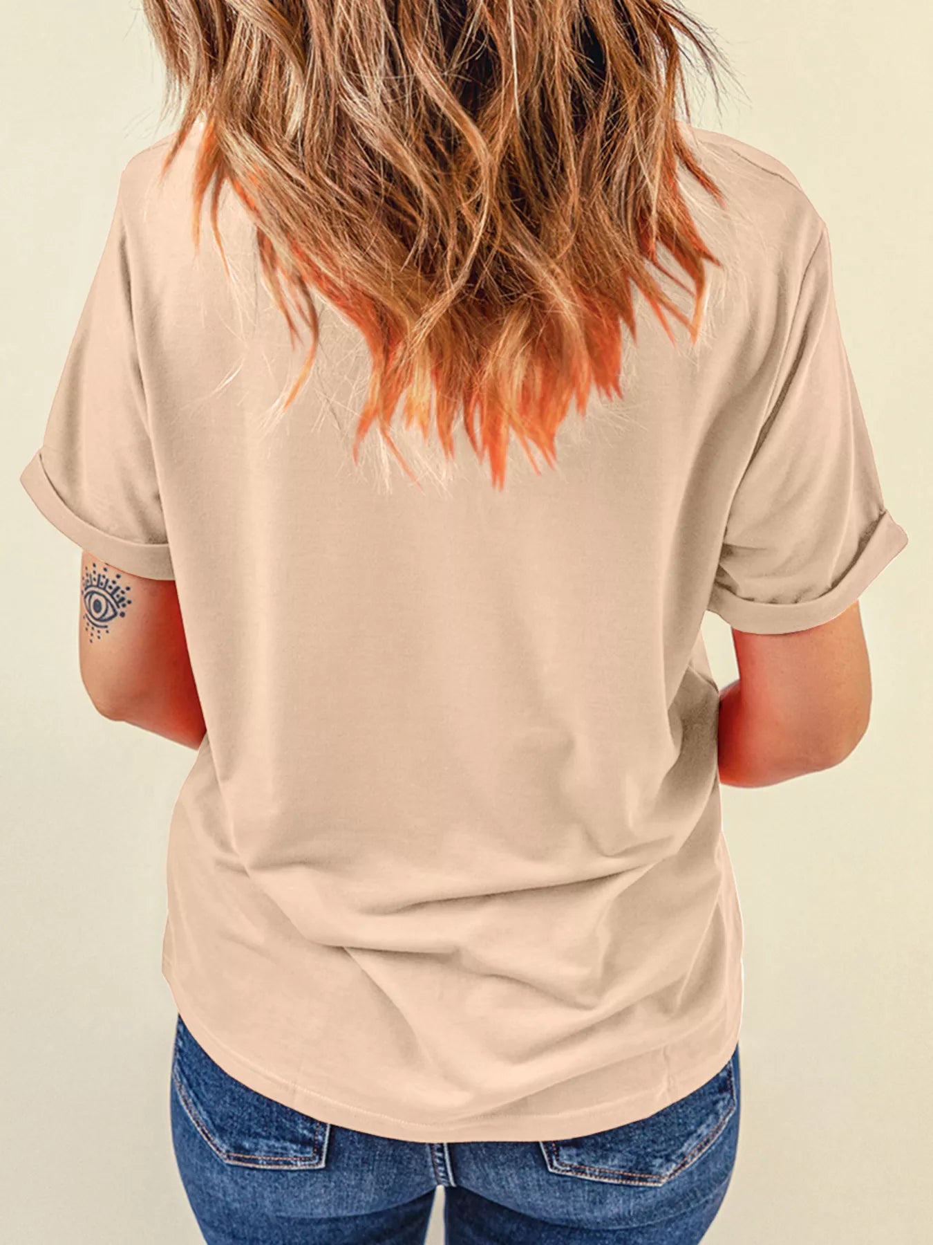 A woman from behind wears a light beige t-shirt and blue jeans.