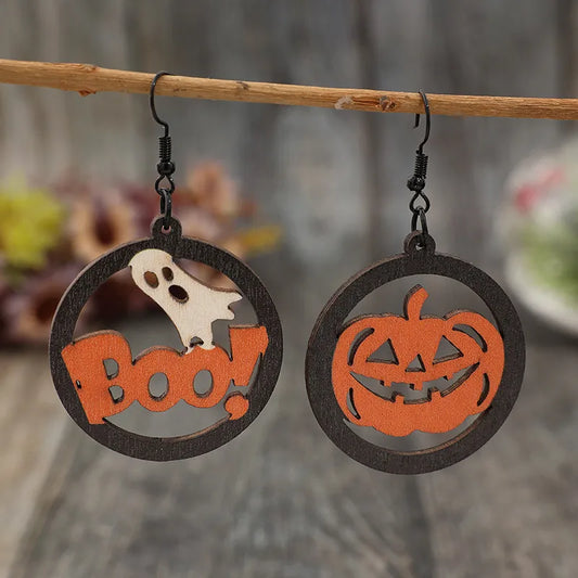 Hollow pumpkin and letter wooden earrings hanging from a branch.