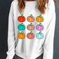 A woman wears a white long-sleeve sweatshirt with a colorful pumpkin graphic.