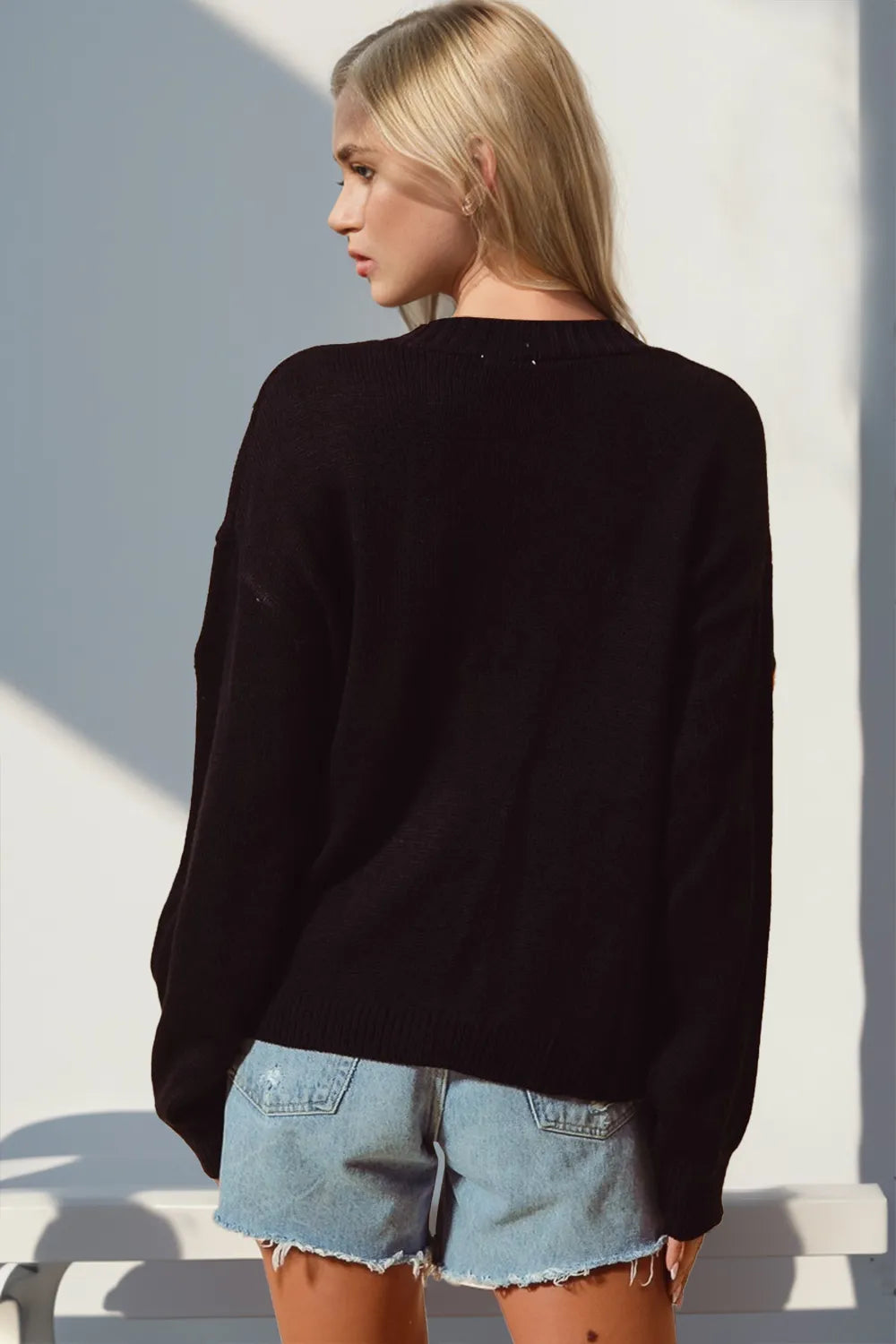 Woman in a black long-sleeve cardigan and denim shorts, viewed from behind.