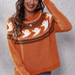 A woman smiles wearing an orange ghost pattern round neck long sleeve sweater.