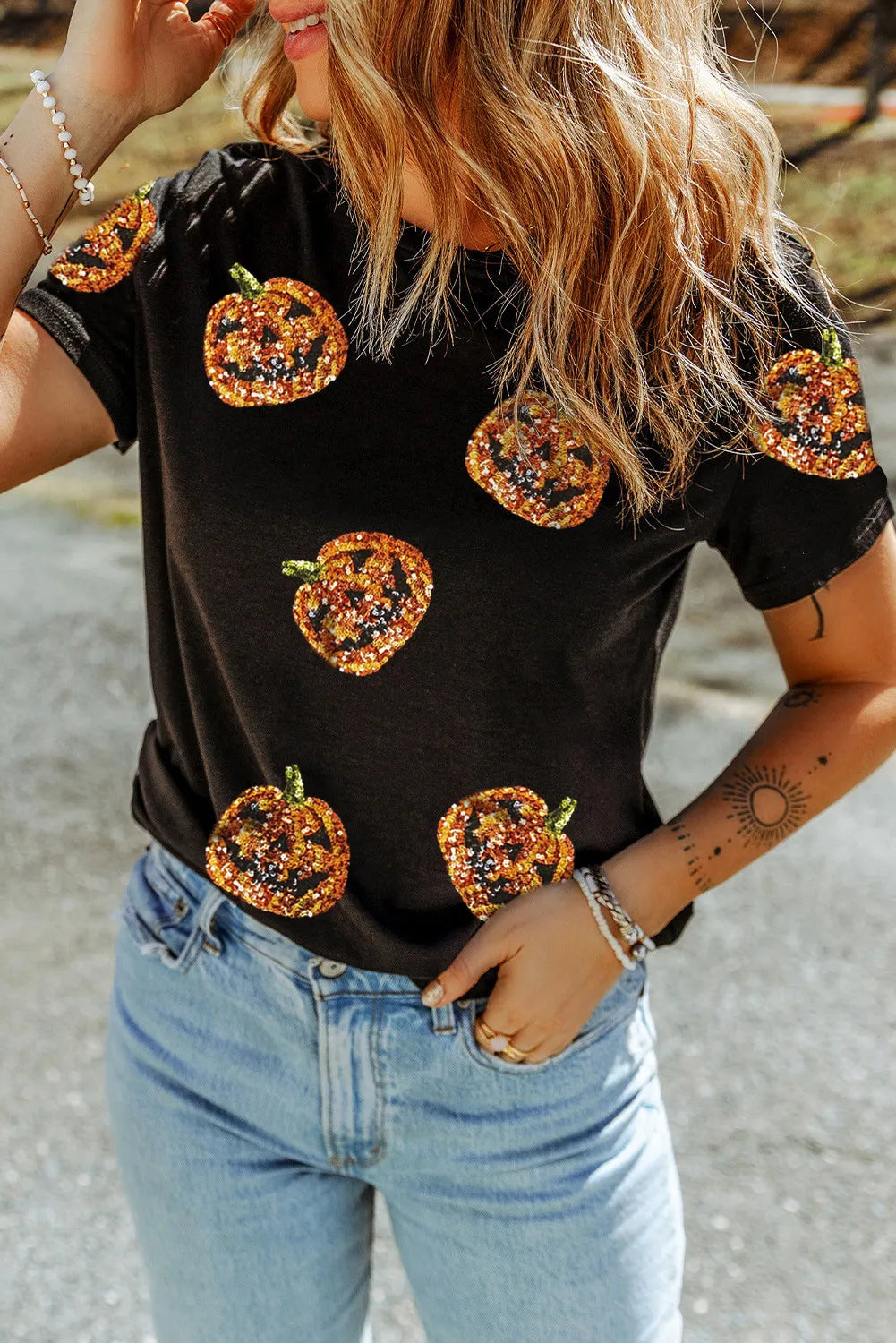 A woman wears a black short-sleeve t-shirt with sequin pumpkin designs.