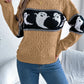 A woman wears a tan long-sleeve sweater with a black and white ghost pattern.