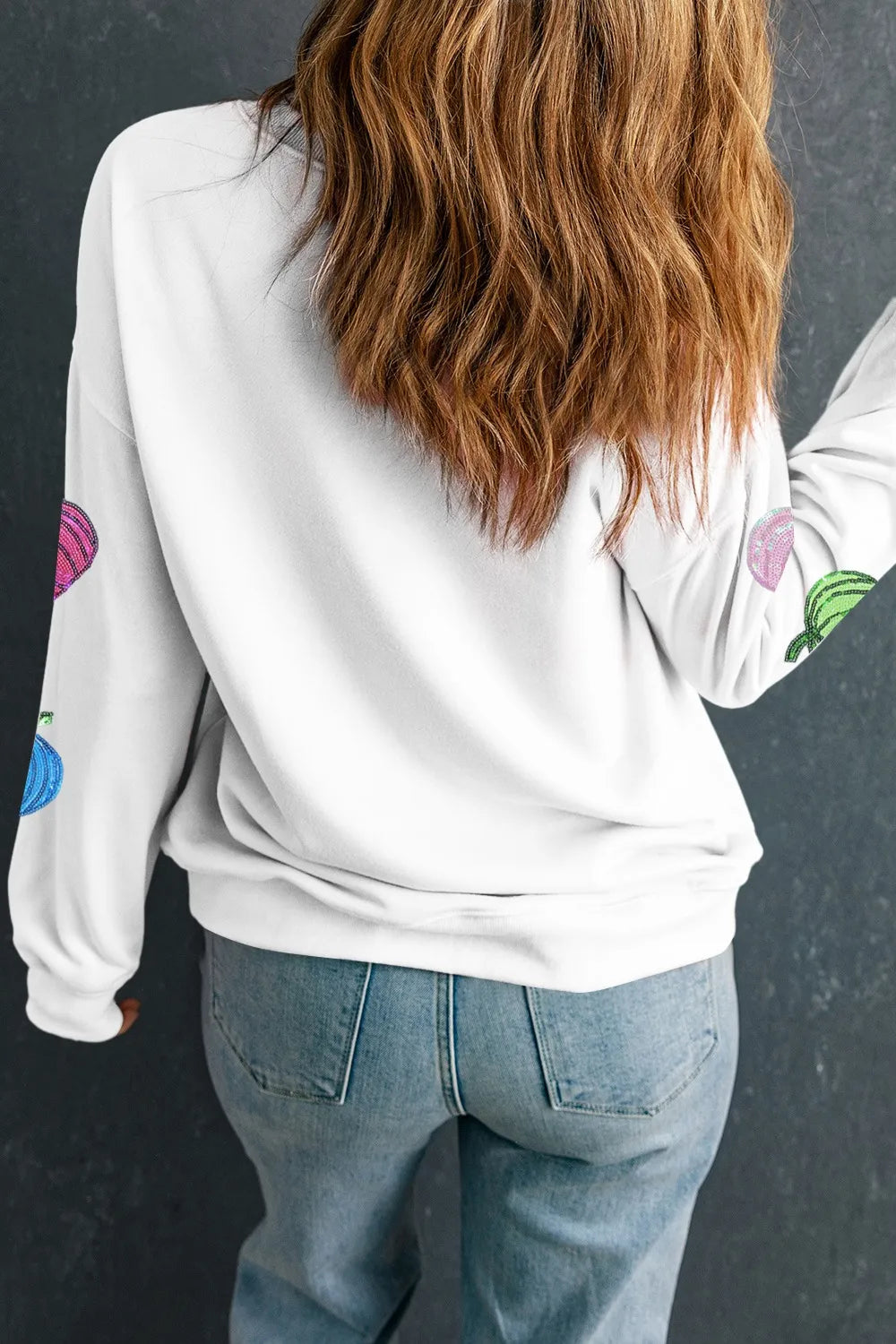A woman from behind wears a white long-sleeve sweatshirt with colorful pumpkin designs.