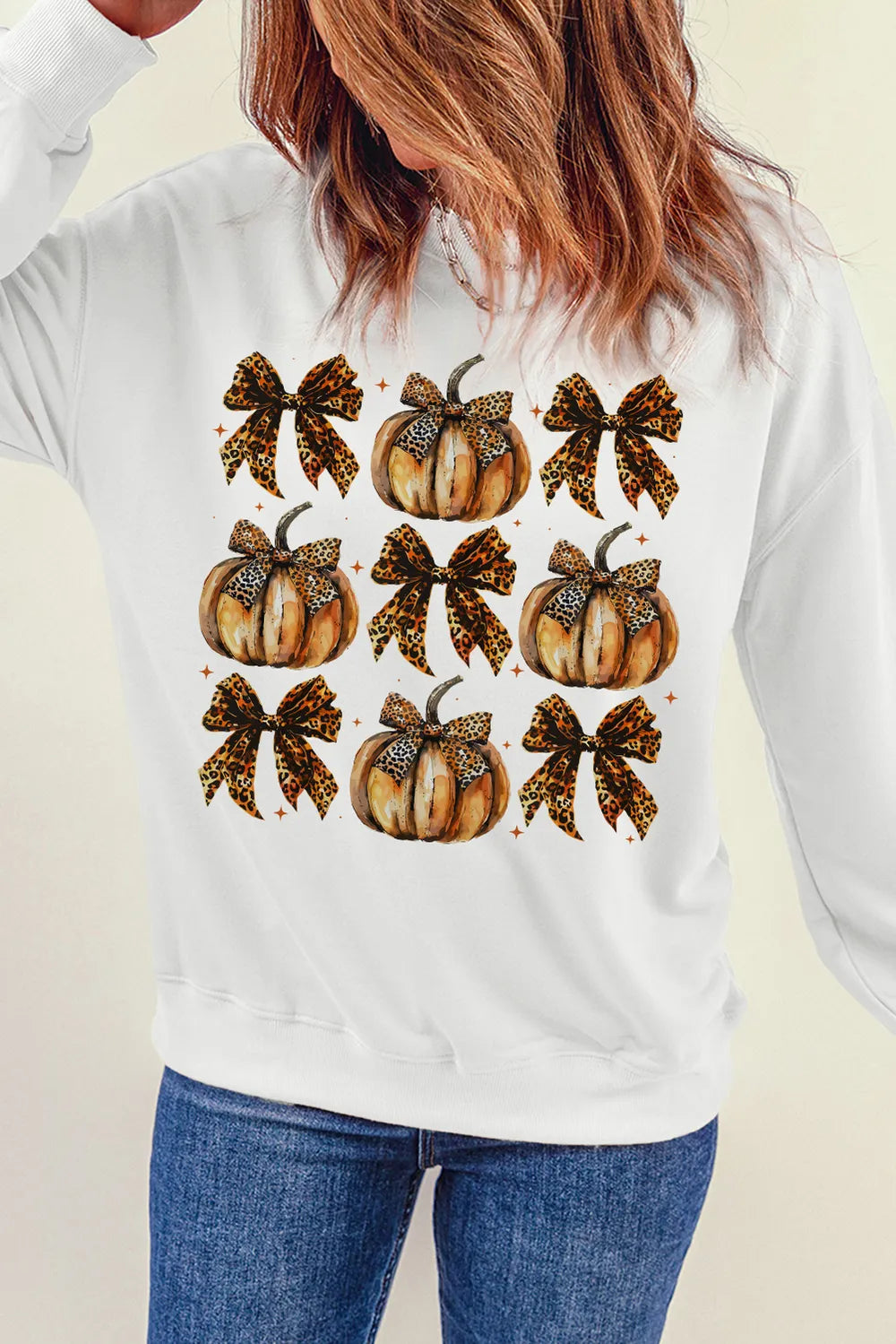 A woman wears a white long-sleeve sweatshirt with a pumpkin and leopard print bow graphic.