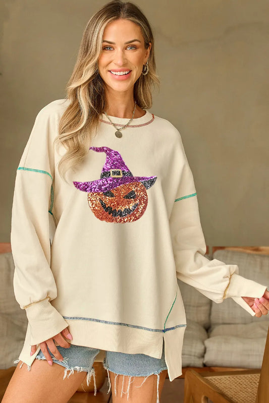 A woman wears a cream sweatshirt with a sequin pumpkin and witch hat design.