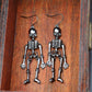 Two dark silver-toned skeleton alloy earrings hang against a wooden background.