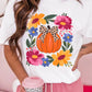 A woman wears a white t-shirt with a pumpkin and floral graphic.
