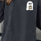 A woman wears a dark gray drop-shoulder sweatshirt with a ghost graphic holding coffee.