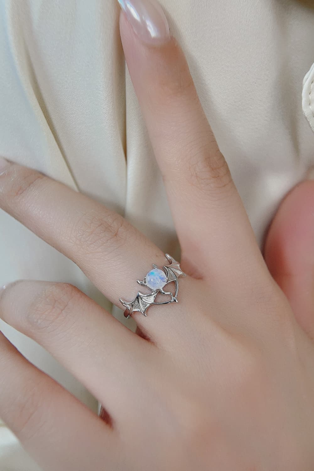 A silver bat ring with a moonstone center is worn on a finger.