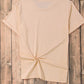 A plain peach short sleeve t-shirt with a knotted hem is displayed on a wooden background.