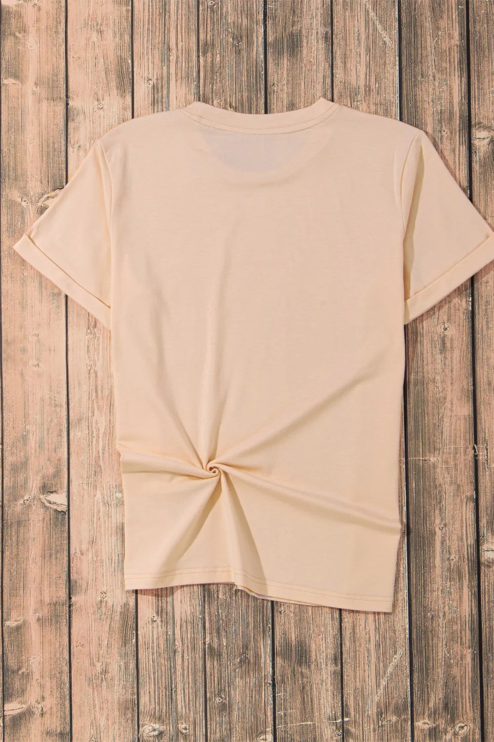 A plain peach short sleeve t-shirt with a knotted hem is displayed on a wooden background.