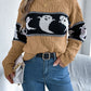 A woman wears a tan, long-sleeve sweater with a black and white ghost pattern.