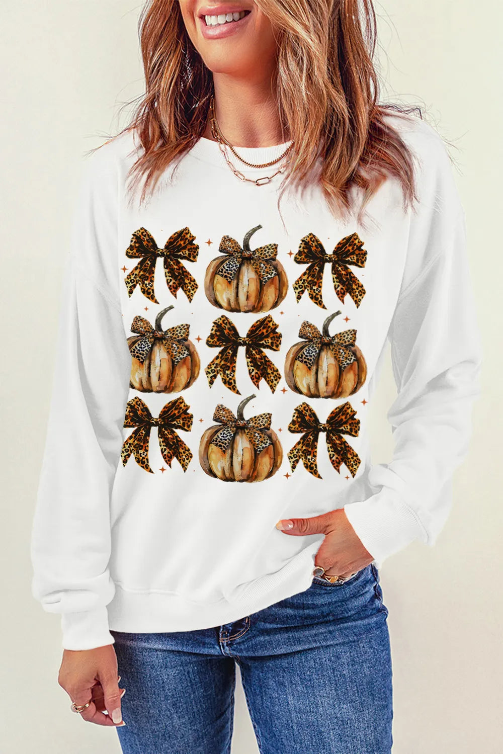 A woman wears a white long-sleeve sweatshirt with a pumpkin and bow graphic.