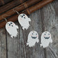 Four ghost-shaped dangle earrings, two with black eyes and pink cheeks, and two with smiling jack-o'-lantern faces.