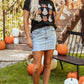 A woman wears a black Halloween graphic t-shirt with a light wash denim skirt.