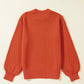 A pumpkin-colored round neck sweater with long balloon sleeves is shown from the back.