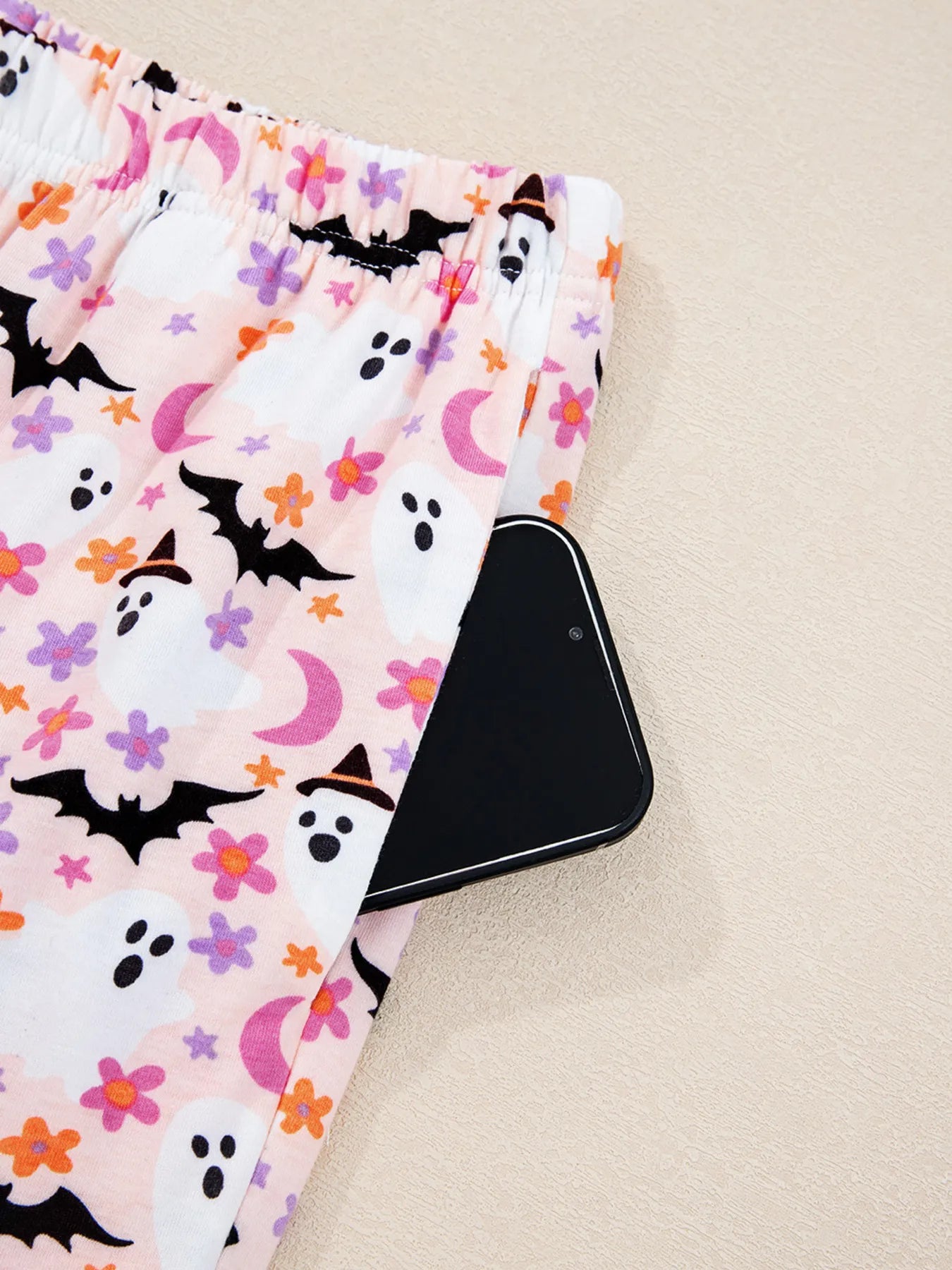 Pink Halloween ghost print pants with a phone in the pocket.
