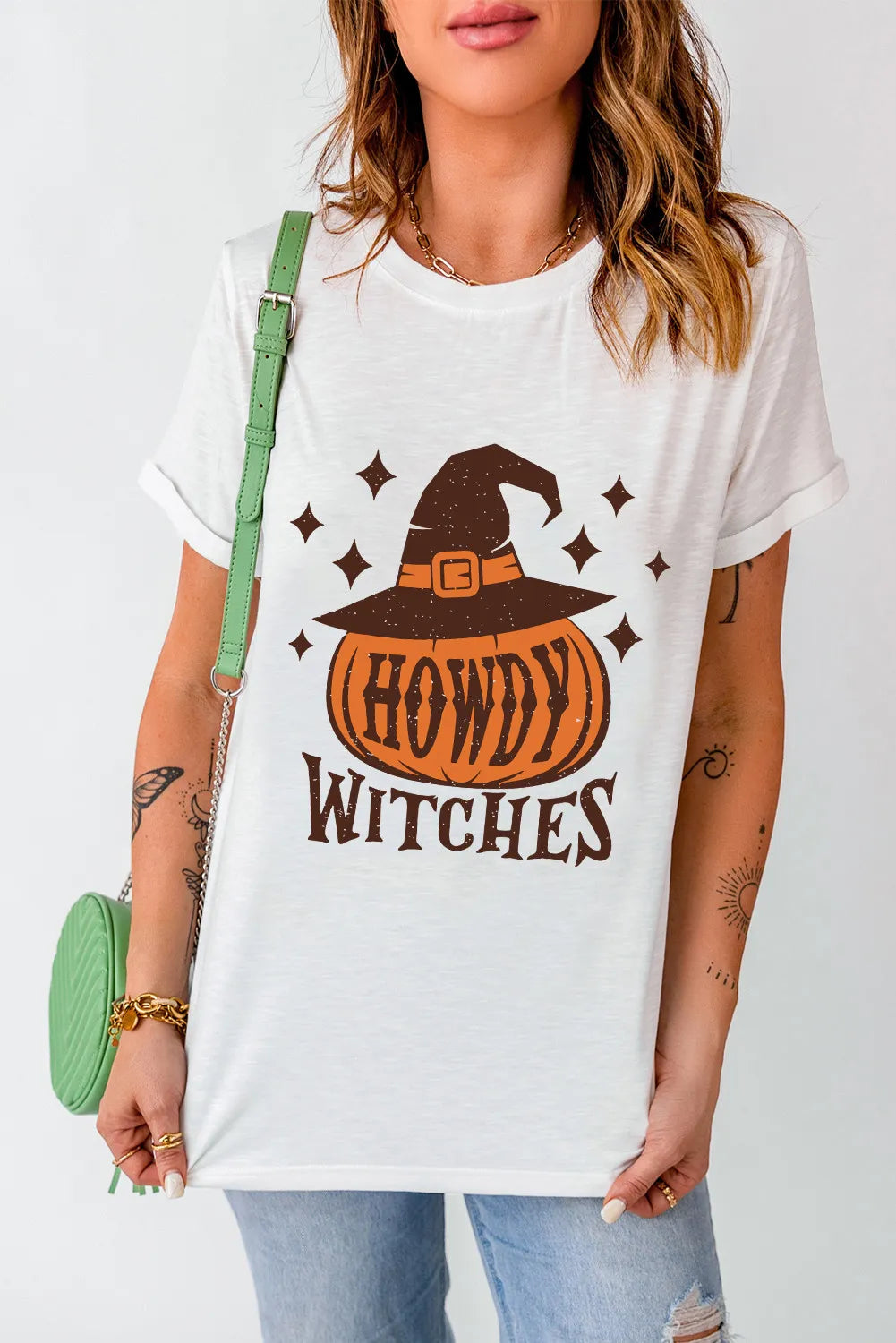 A woman wears a white "Howdy Witches" t-shirt with a pumpkin and witch hat design.
